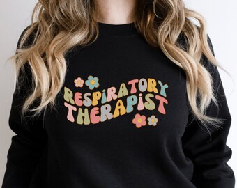 May include: Black sweatshirt with the words "RESPIRATORY THERAPIST" in a retro, colorful font. The design includes flowers in pastel colors. A casual, comfortable top for respiratory therapists.