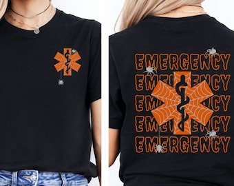 Op de afbeelding: Zwart T-shirt met een Halloween-ontwerp. De voorkant heeft een oranje star of life-symbool met een spinnenweb en een kleine spin. De achterkant van het shirt herhaalt het woord "NOODGEVAL" met het star of life-symbool en spinnen.