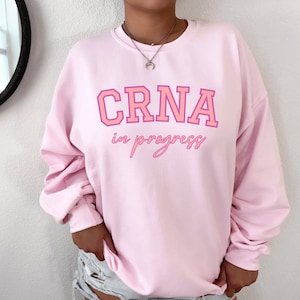 May include: Pink sweatshirt with the text "CRNA in progress" in pink lettering.