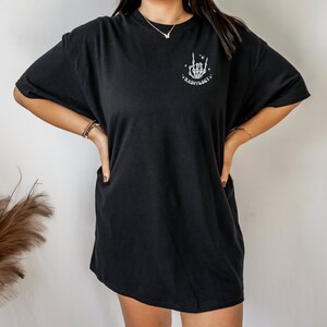 May include: Black oversized t-shirt with a white graphic of a skeleton hand making a rock and roll sign. The graphic also includes the text "Radiology".