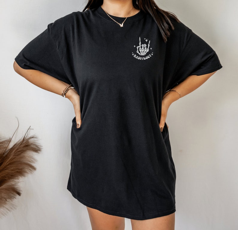 May include: Black oversized t-shirt with a white graphic of a skeleton hand making a rock and roll sign. The graphic also includes the text "Radiology".
