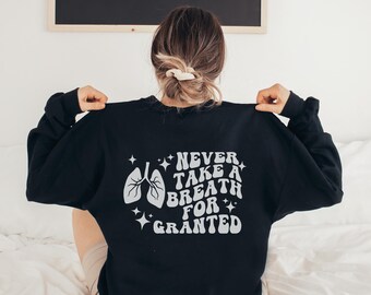 May include: Black sweatshirt with a white graphic print that says "Never take a breath for granted" with a stylized image of lungs.