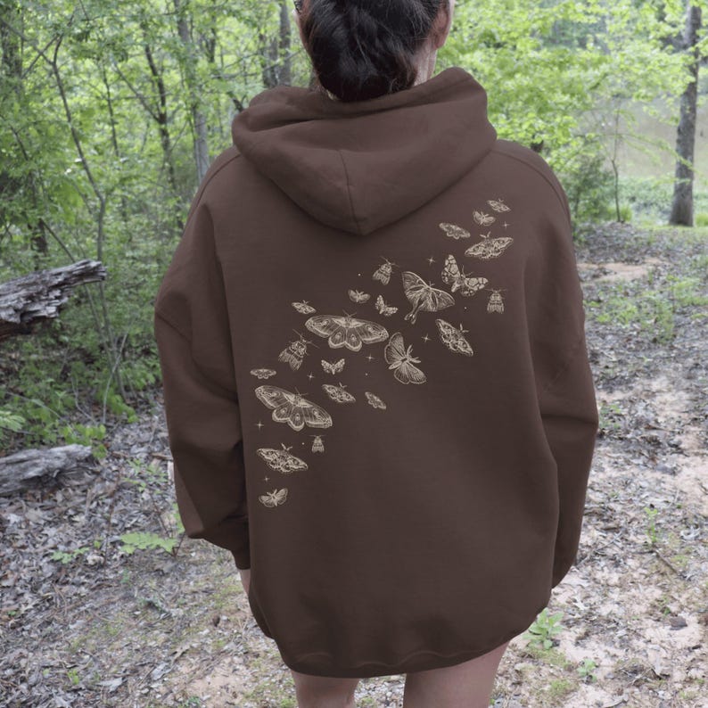 May include: A brown hoodie with a design of moths and butterflies on the back. The design is in a light tan color and features various sizes and shapes of moths and butterflies. The hoodie has a hood and a kangaroo pocket.