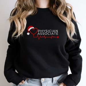 Könnte beinhalten: Schwarzer Pullover mit einem roten Herzen, auf dem ein Weihnachtsmann-Hut sitzt. Unter dem Herzen steht der Text "PHYSICIAN ASSOCIATE" mit einer roten EKG-Linie.