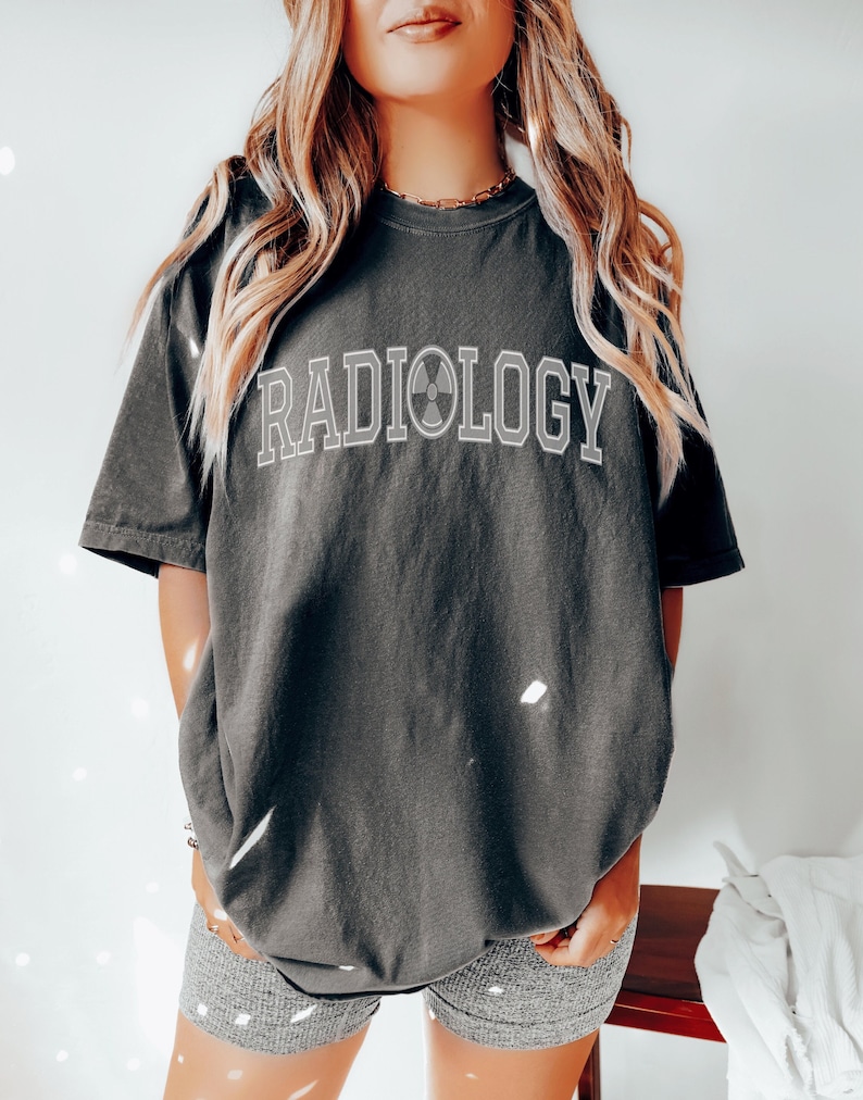 May include: A dark gray t-shirt with the word "RADIOLOGY" printed in white with a gray radiation symbol in the middle of the word.