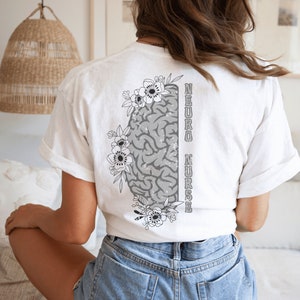 May include: White t-shirt with a gray brain graphic and floral accents. The text "NEURO NURSE" is printed vertically on the right side of the brain graphic.