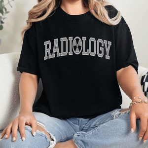 May include: Black t-shirt with the text "RADIOLOGY" in white with a gray radiation symbol in the middle of the word.