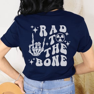 May include: Navy blue t-shirt with a white skeleton hand giving the middle finger, a radioactive symbol, and the text "Rad to the Bone" in a retro font.