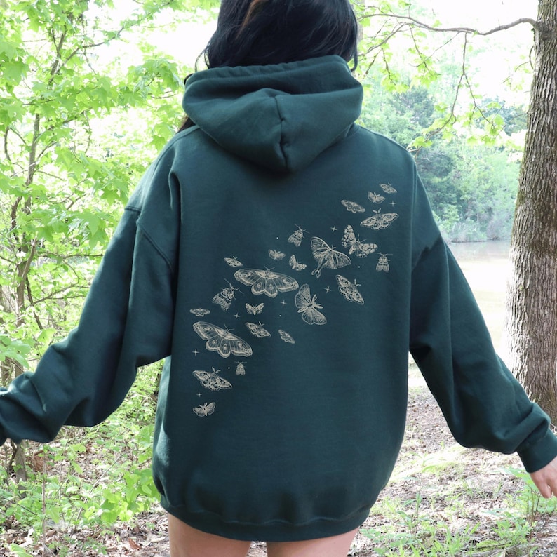 May include: Dark green hoodie with a hood and long sleeves. The back of the hoodie features a design of various moths and butterflies in a light tan color. The hoodie is made of a soft material.