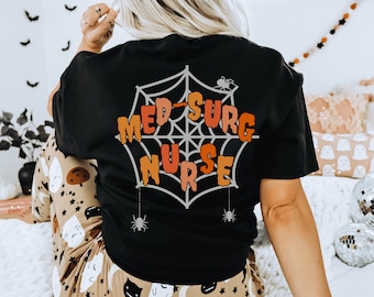 May include: Black t-shirt with a spiderweb graphic and the text "Med-Surg Nurse" in orange and red lettering.