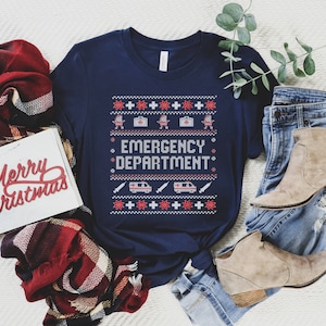 May include: A navy blue t-shirt with a white and red pixelated design featuring a medical symbol, a first aid kit, a medical van, and the text "Emergency Department".