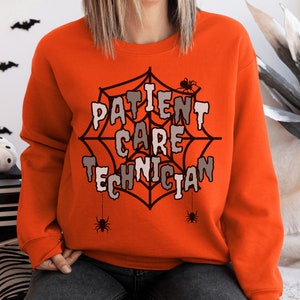 May include: Orange sweatshirt with the words "PATIENT CARE TECHNICIAN" in a web design, with spiders. The sweatshirt is a crew neck style. The design is in white, gray, and black. The sweatshirt is a Halloween theme.