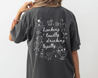 Puede incluir: Camiseta gris oscuro con un gráfico blanco de patos de dibujos animados con bebidas y el texto "honking loudly drinking legally."