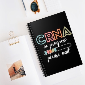 May include: Black spiral notebook with the text "CRNA in progress please wait" in colorful letters. A progress bar with five colored circles is below the text.