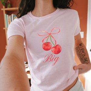 May include: Pink cropped t-shirt with a graphic of two red cherries with a pink bow and the word "Big" in pink script.