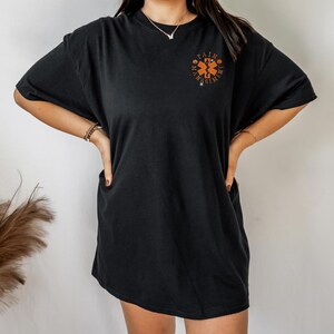 May include: Black oversized t-shirt with an orange graphic of a medical symbol and the text "Pain Management".