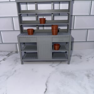 Puede incluir: Una despensa de madera gris con estantes y un armario. La despensa tiene cuatro pequeñas macetas de terracota en los estantes.