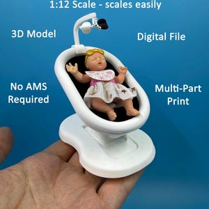 May include: A white 3D printed miniature baby swing for a dollhouse in 1:12 scale. The swing features a black seat and a small mobile attachment. A miniature baby doll with blonde hair, a floral bib, and a white dress with gold stars sits inside.