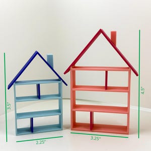 Könnte beinhalten: Zwei Miniatur-Regale in Hausform. Eines ist blau mit blauem Dach, 8,9 cm hoch und 5,7 cm breit. Das andere ist korallenfarben mit rotem Dach, 11,4 cm hoch und 8,3 cm breit. Beide haben Regalböden.