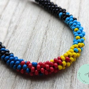 May include: A close-up of a beaded necklace with black, blue, red, and yellow beads. The beads are arranged in a spiral pattern.