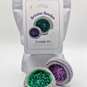 May include: A crochet kit for making two "Arcane Geodes" with a gray, green, and purple color scheme. The kit includes materials for sensory play. The packaging features the text "A Parlin Project" and "Crochet Kit".