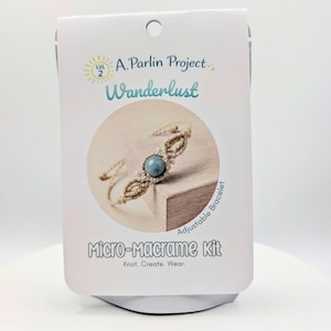 以下が含まれることがあります： A. Parlin Project Wanderlustとラベル付けされたマイクロマクラメキット用の白い長方形のパッケージカード。カードには、中央に青い石のビーズが付いたベージュのマクラメブレスレットの円形の画像と、Knot. Create. Wear.というテキストが記載されています。