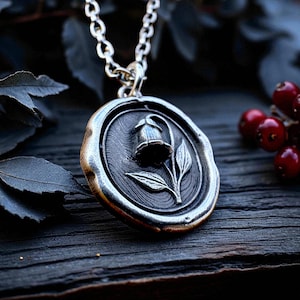 Sterling silver wax seal pendant featuring the belladonna flower, shown at an angle on dark wood with berries and leaves