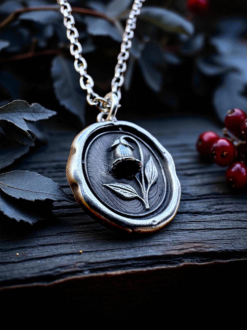 Sterling silver wax seal pendant featuring the belladonna flower, shown at an angle on dark wood with berries and leaves