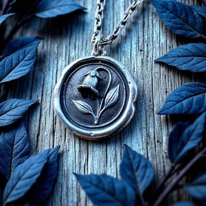 May include: A silver pendant necklace featuring a detailed floral design. The pendant, with a flower and leaves, hangs from a chain. The image is set against a wooden background with blue leaves, creating a nature-inspired aesthetic.