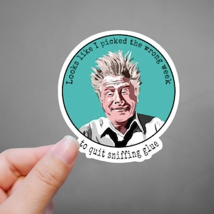 May include: A round sticker with a turquoise background featuring a cartoon illustration of a man with messy white hair and a surprised expression. The text around the image reads "Looks like I picked the wrong week to quit sniffing glue."