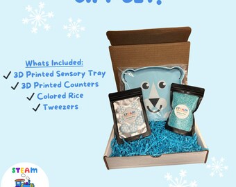May include: A blue and white gift set for sensory play includes a 3D printed sensory tray, 3D printed counters, colored rice, and tweezers. The set is packaged in a brown box with blue and white tissue paper. The box is labeled "STEAM Indoor Play Center".