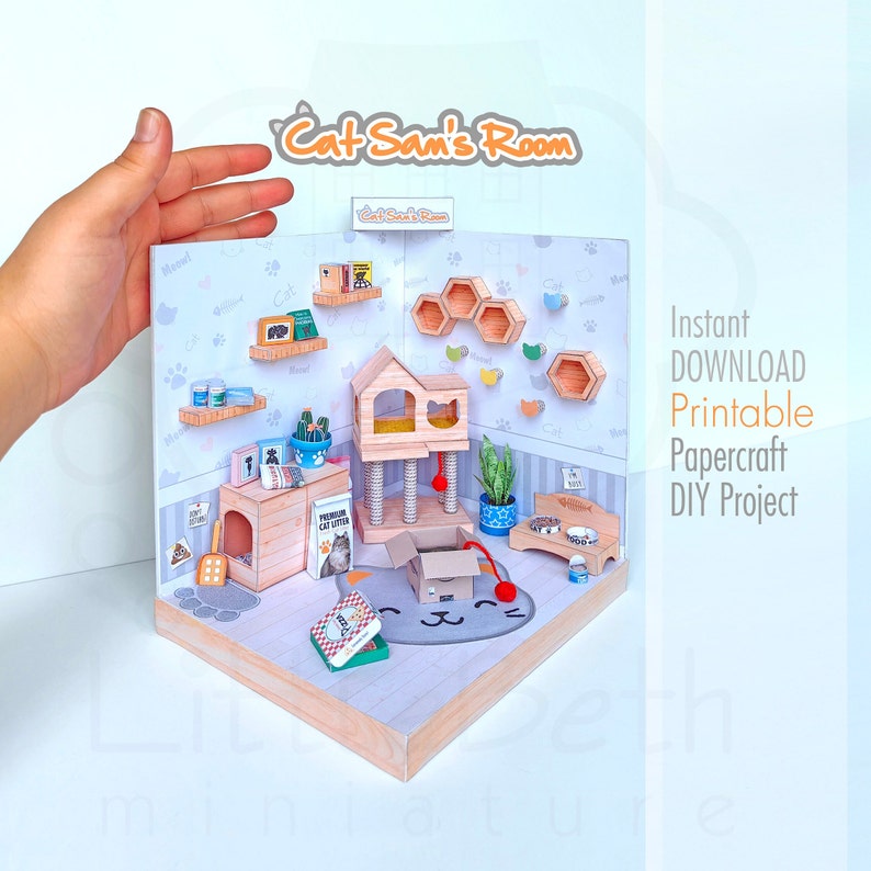 Op de afbeelding: Een printbaar papiercraft DIY-project van een kattenkamer. De kamer heeft een kattenboom, een kattenbed, een krabpaal en een verscheidenheid aan katten speelgoed. De kamer is versierd met een katten-thema behang en een kattenvormig tapijt. Het project heet "Cat Sam's Room".