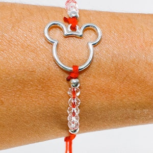 May include: A red string bracelet featuring a silver-toned metal outline of a mouse head silhouette. The bracelet is accented with small, clear, faceted beads and silver-toned metal spacers, tied with a simple adjustable red cord closure.