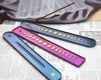 May include: Three iridescent resin incense holders with moon phases and stars designs. The holders are in shades of blue, purple, and pink.