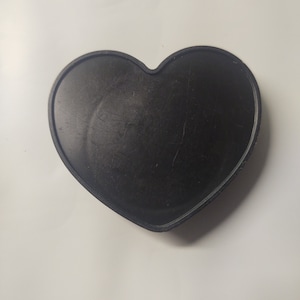 Op de afbeelding: Een zwarte hartvormige dienblad gemaakt van glad, hard materiaal. Het dienblad is perfect om kleine voorwerpen te presenteren of snacks te serveren.