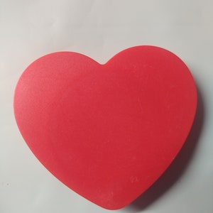 Op de afbeelding: Een felrood hartvormig object van plastic. Het hart is glad en heeft een licht glanzende afwerking.
