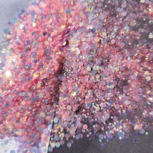 May include: Pink and iridescent glitter with a holographic finish. The glitter is scattered on a white and black surface.
