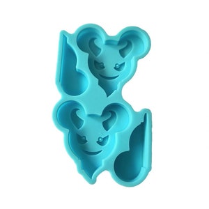 May include: A light blue silicone mold featuring two cartoon devil mouse faces. Each face has curved horns, a sinister smile, and pointed eyes. The mold is designed for crafting or baking, with a smooth surface and a unique shape.