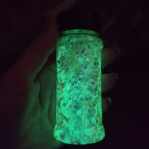 May include: A clear glass jar filled with iridescent glitter that glows green in the dark.