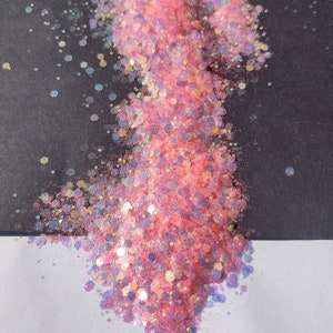 May include: Pink and iridescent glitter with a holographic finish. The glitter is scattered on a black and white surface.