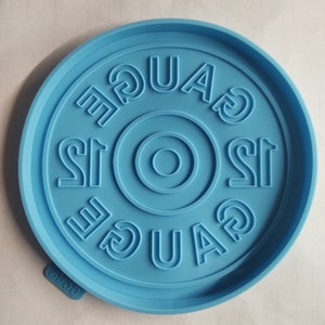 May include: A light blue silicone coaster with the word "Gauge" embossed around the edge. The center of the coaster has a circle with a smaller circle inside.