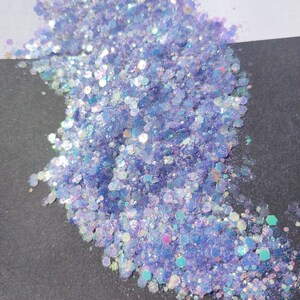 May include: A pile of iridescent purple glitter with a holographic finish. The glitter is scattered on a black surface.