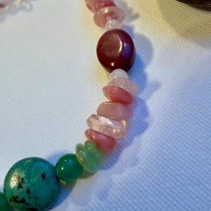 Può includere: Un braccialetto di perline con una varietà di pietre preziose colorate. Il braccialetto include perline turchesi, verdi, rosa e bordeaux. Le perline sono infilate su una catena d'argento con una chiusura.