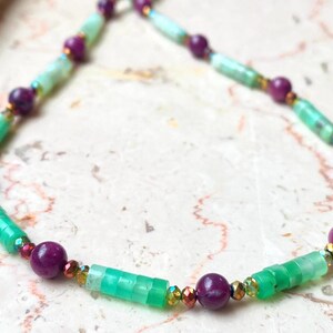 Può includere: Una collana di perline verdi e viola con un mix di perline rotonde e rettangolari. La collana è realizzata con pietre naturali e ha uno stile delicato e bohémien.