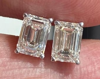 Könnte beinhalten: Ein Paar Ohrstecker mit Diamanten im Smaragdschliff. Die Diamanten sind in einer Fassung aus Silber oder Weißgold gefasst. Die Ohrringe werden im Nahaufnahme gezeigt, wobei die Diamanten das Licht reflektieren.