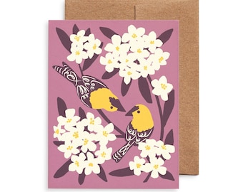 May include: A greeting card with a mauve background features two yellow birds with black and white details, surrounded by white flowers and dark purple leaves. The card is paired with a brown envelope, creating a nature-inspired design.