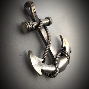May include: A silver-toned metal anchor pendant featuring a textured rope wrapped around the shank and flukes. The top bail is stamped with the number 925 and an infinity symbol, indicating sterling silver composition and a nautical design aesthetic.