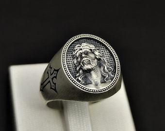 May include: A silver ring with a black cross design on one side and a detailed image of Jesus on the other side.