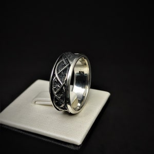 May include: A silver ring featuring a Celtic knot design. The ring is displayed on a white stand.