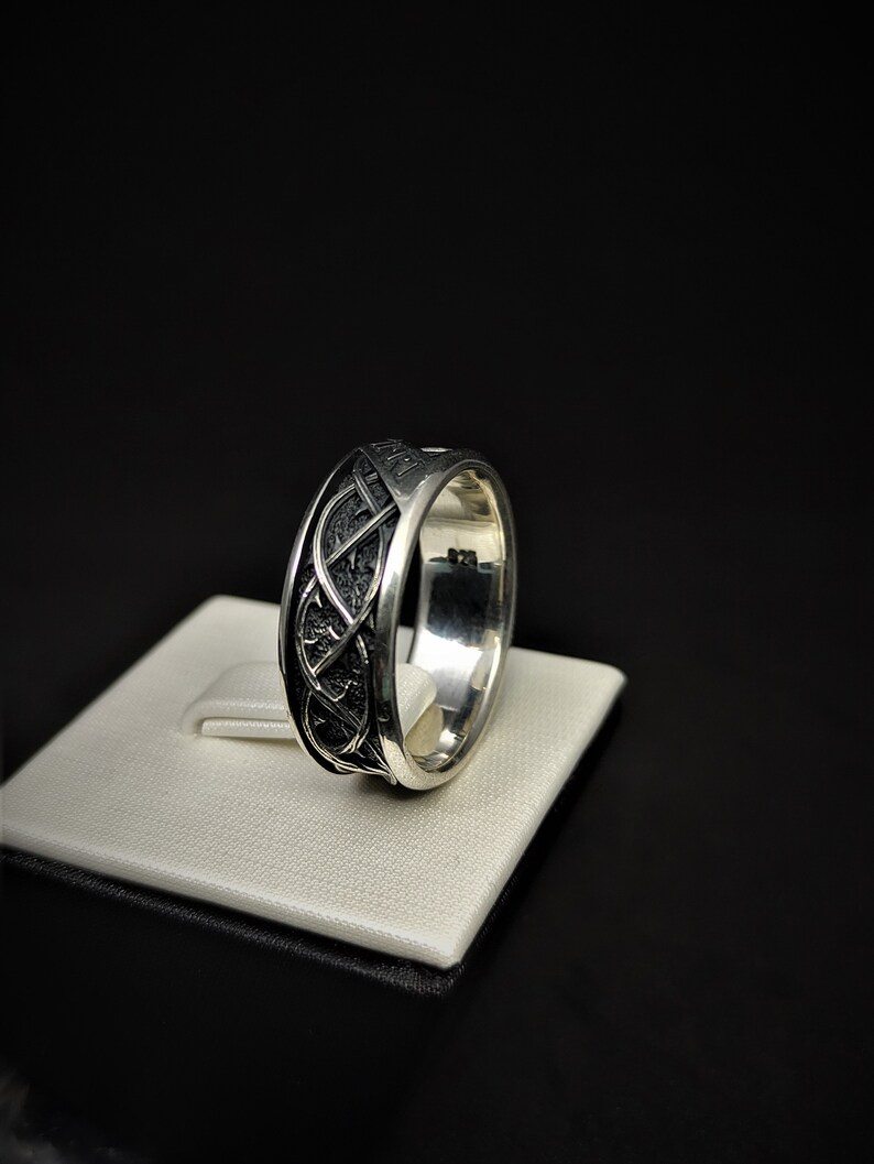 May include: A silver ring featuring a Celtic knot design. The ring is displayed on a white stand.